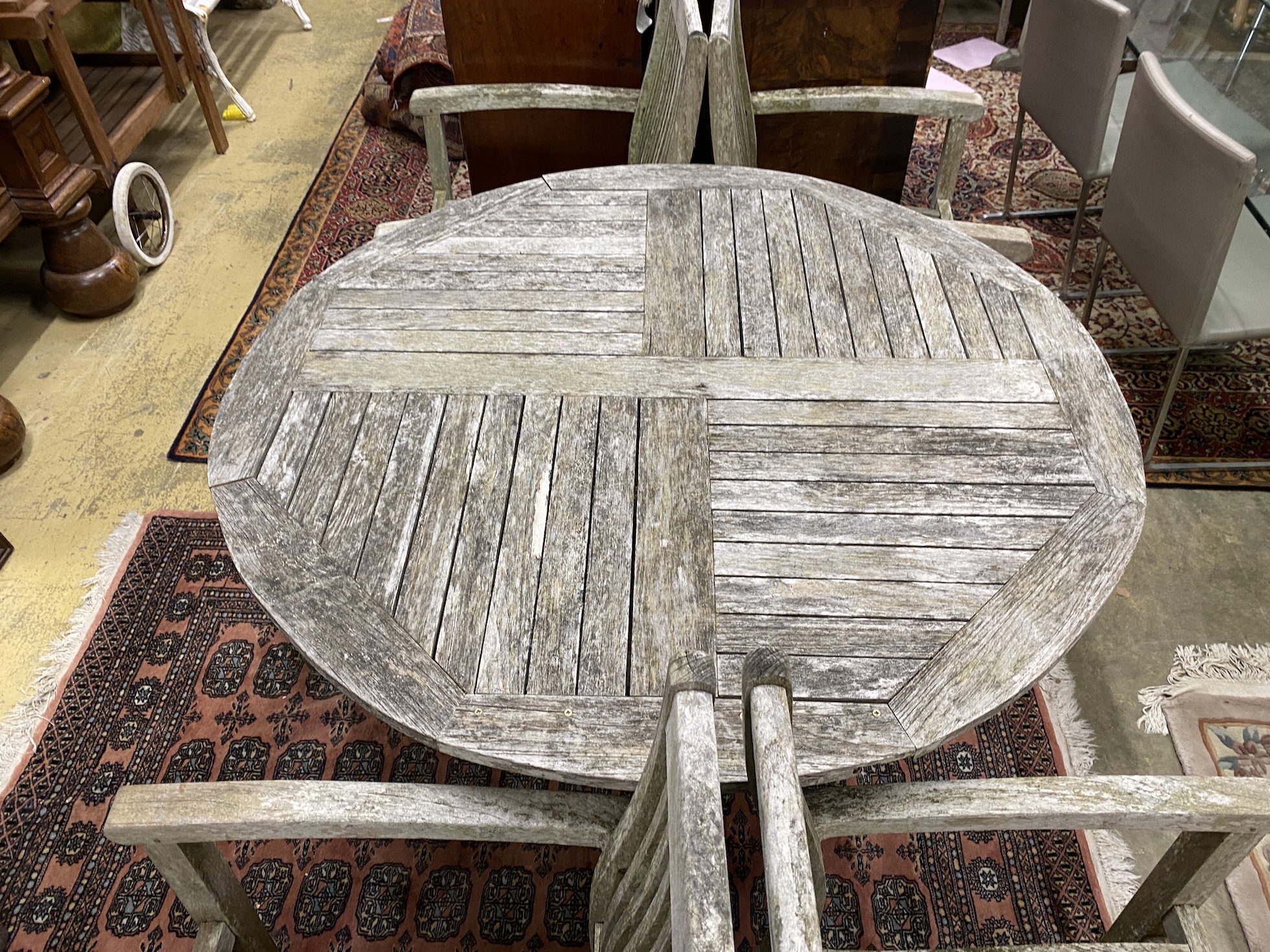 A circular weathered teak garden table, diameter 120cm, height 75cm and four elbow chairs